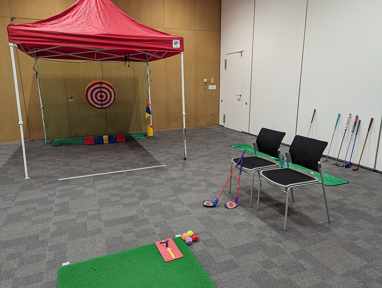 A simple indoor golf practice setup in Japan with a net, target, and putting mat