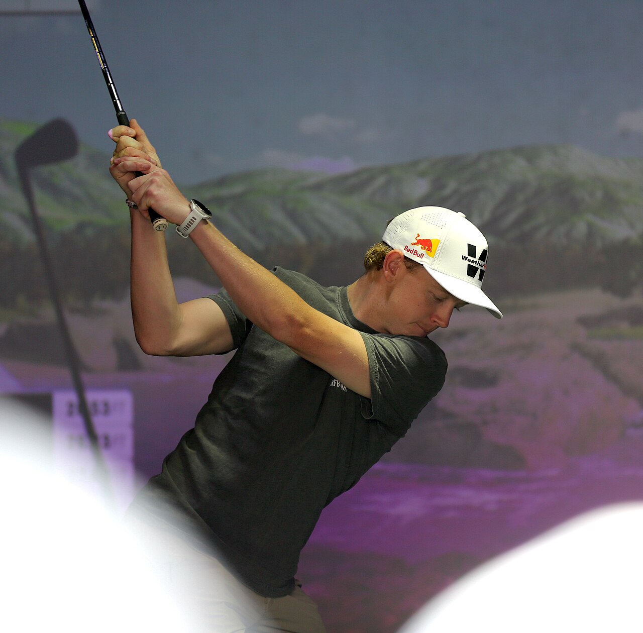 A golfer mid-swing in front of a golf simulator screen showing a virtual course
